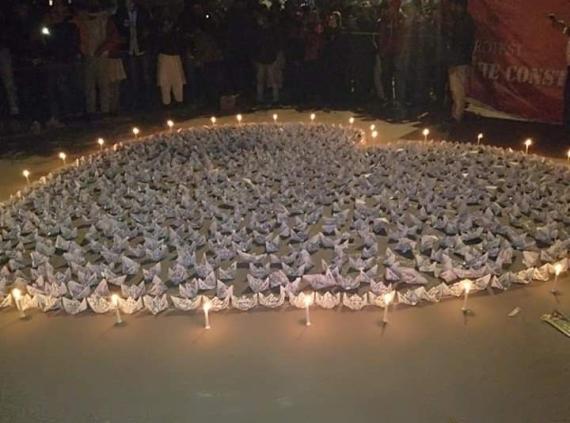 Paper cranes laid out in the shape of a heart with candles surrounding