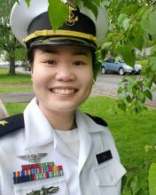 An image of Tran Huynh Bao Ho, smiling and in uniform, against a backdrop of green leaves. 