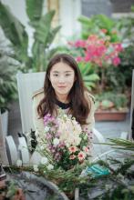 An image of Jieyu Zhou seated in a white chair with flowers on a table in the foreground