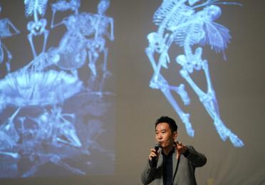 Prof. Ungsan Kim delivers a lecture against a backdrop of slides showing x-rays of skeletons
