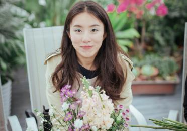 An image of Jieyu Zhou seated in a white chair with flowers on a table in the foreground