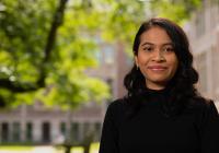 An image of Anselma Prihandita, wearing a black turtleneck and standing against a backdrop of the quad