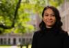 An image of Anselma Prihandita, wearing a black turtleneck and standing against a backdrop of the quad
